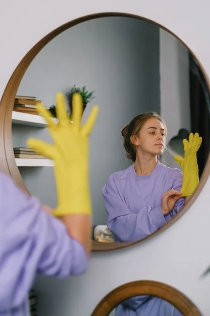 Close-up of hand cleaning window with squeegee outdoors using yellow gloves.